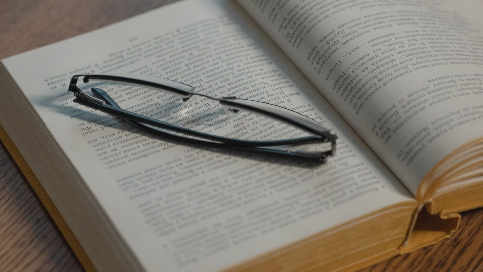 Очки для чтения на раскрытой книге с кириллическим текстом, деревянный стол
